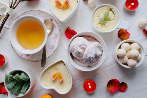 Free A flat lay of desserts and tea with candles and petals on a white background, creating a cozy ambiance. Stock Photo