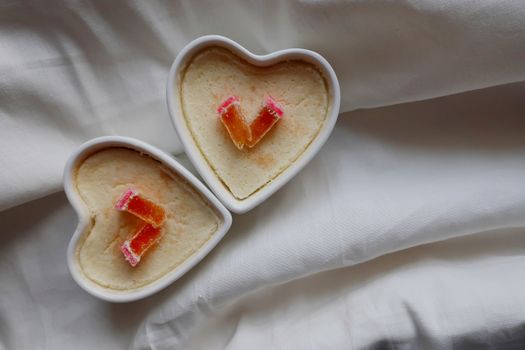Top view of heart shaped curd soufflés in ramekins on white fabric background.