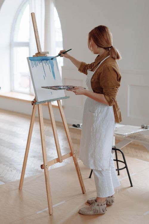 Free Female artist painting on canvas in sunny studio with easel and brush. Stock Photo