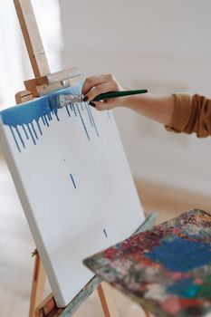 Close-up of hand painting with blue on a canvas using a paintbrush.