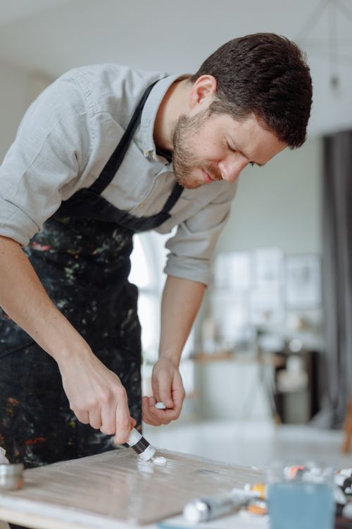 Free A dedicated artist works on a painting in a light-filled studio space, deep in concentration. Stock Photo