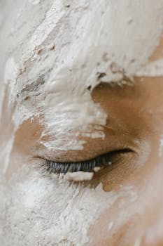 A serene close-up of a closed eye with white clay face mask applied for skincare.