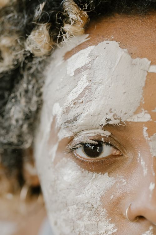 Free Artistic close-up portrait with a clay face mask highlighting texture and eye detail. Stock Photo