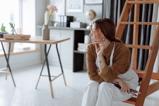 Woman artist in a creative moment, surrounded by art supplies in a well-lit studio.