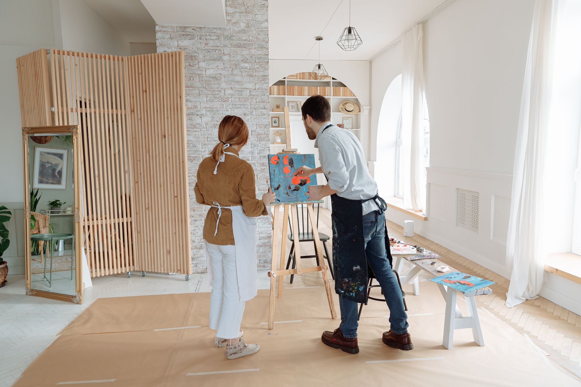 Two artists collaborating on a painting in a well-lit modern studio interior.