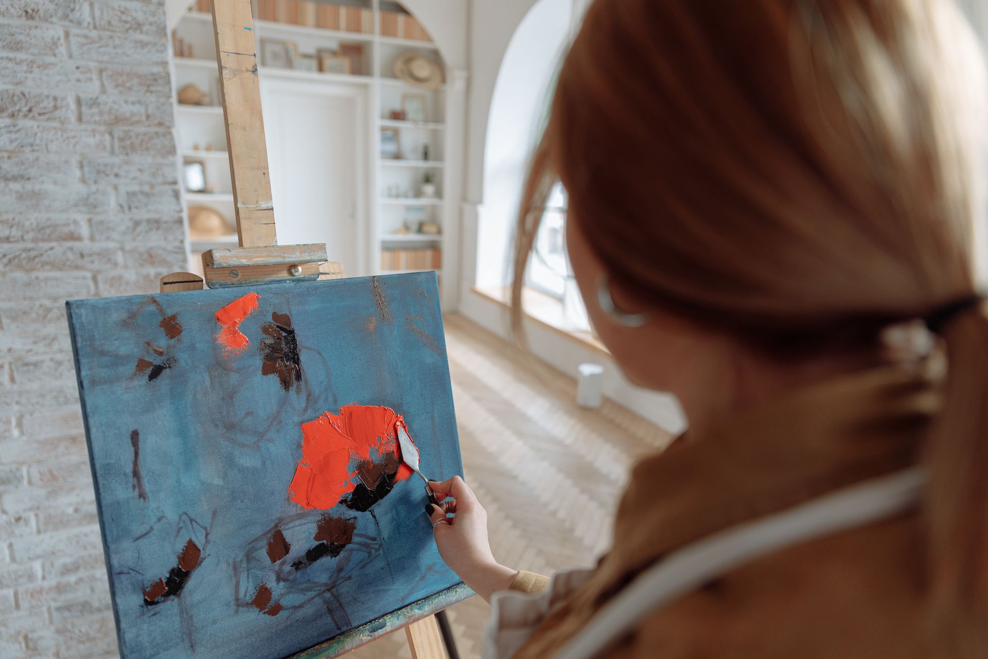 A female artist paints abstract art on canvas using vibrant colors in a cozy studio.