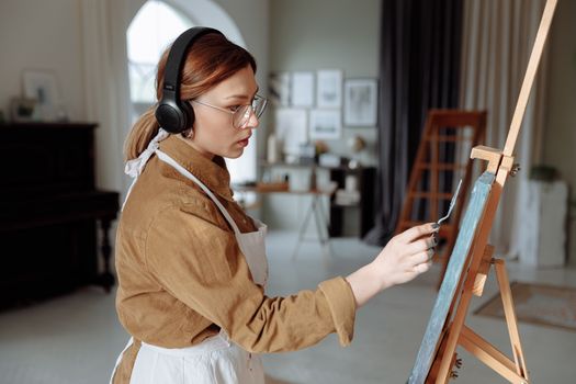 Woman painting with palette knife while listening to music in art studio.