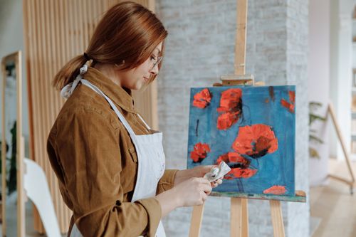 Free A female artist painting vibrant red poppies on a canvas in her studio. Stock Photo