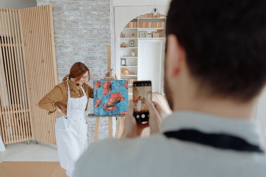 Creative artist posing with a colorful abstract painting in an indoor studio setting.
