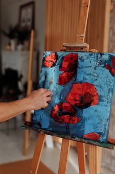 A vibrant oil painting of red poppies being created on an easel with a palette knife.