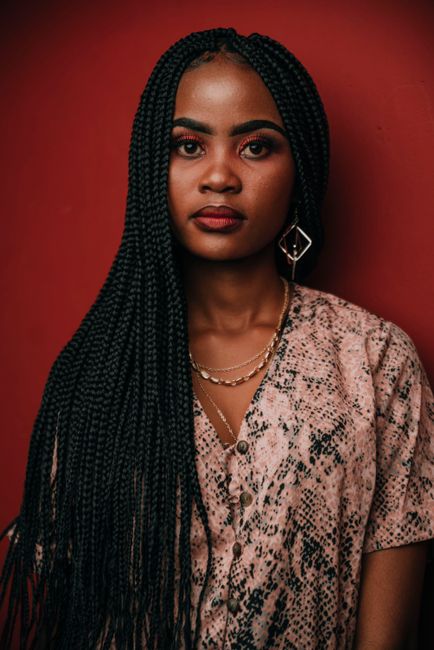 Captivating portrait of a woman with braided hair against a red background, exuding confidence and style.