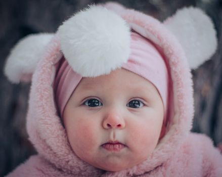 Cute baby in a pink fluffy hoodie with adorable pom pom ears. Close-up portrait.