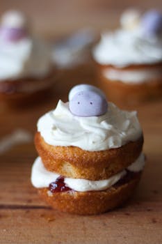 A delightful mini cupcake with cream frosting and berry filling, topped with a purple candy.
