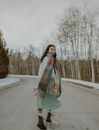 Back view of stylish young Asian female millennial in fashionable outfit running on asphalt road amidst leafless trees and looking over shoulder on cloudy winter day