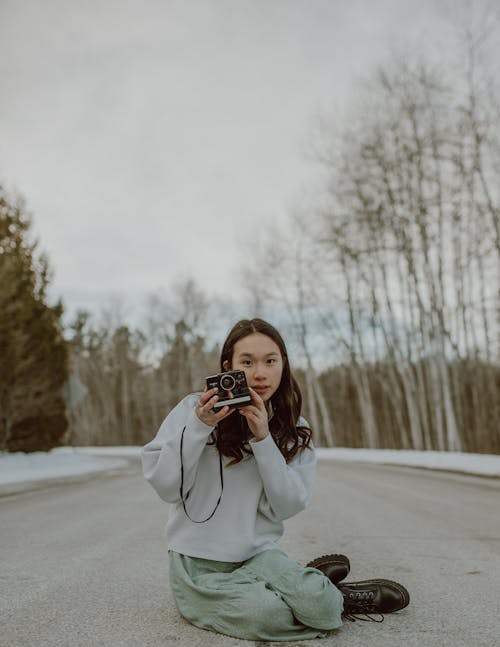 Stylish young Asian female photographer shooting on film camera sitting on road