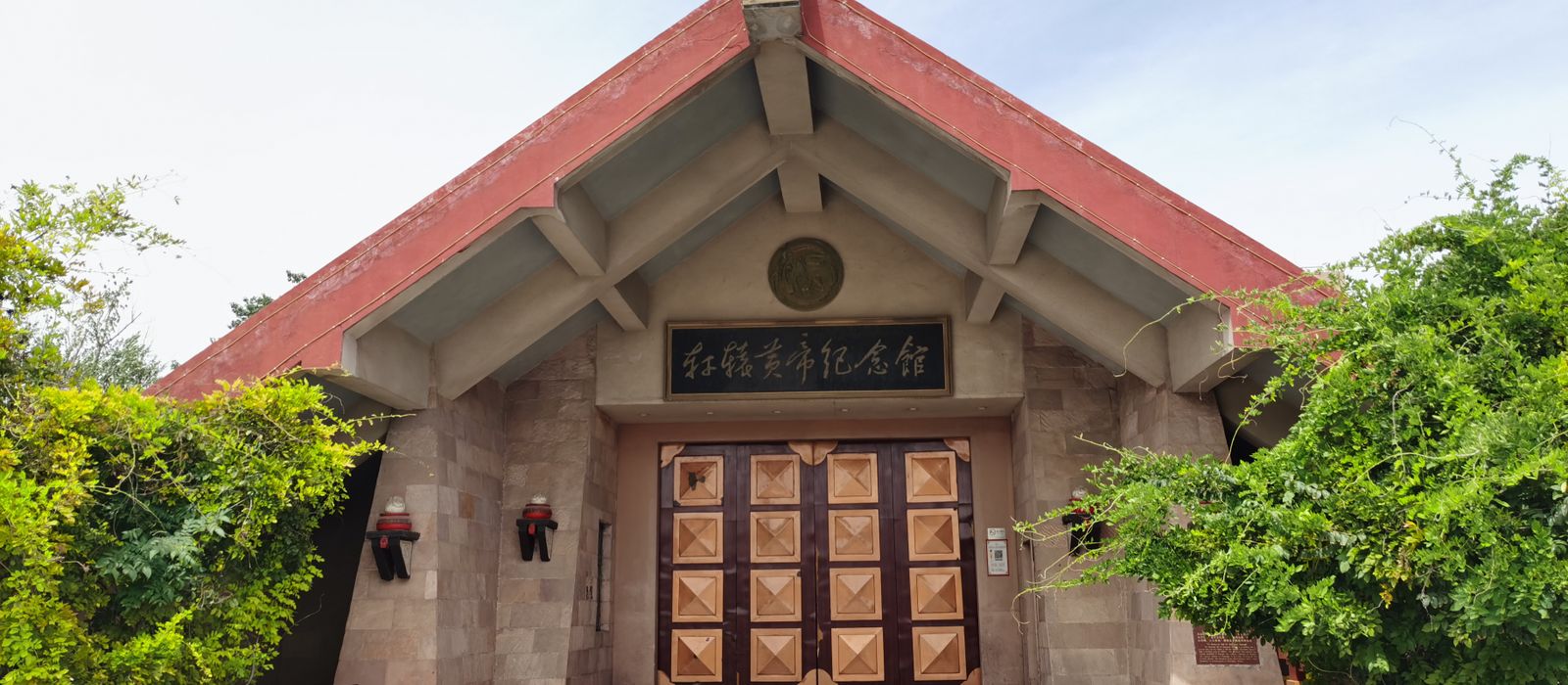 Front view of a traditional building with a wooden door, lush greenery, and a blue sky in Zhengzhou, China. — flights from Guangzhou to Zhengzhou