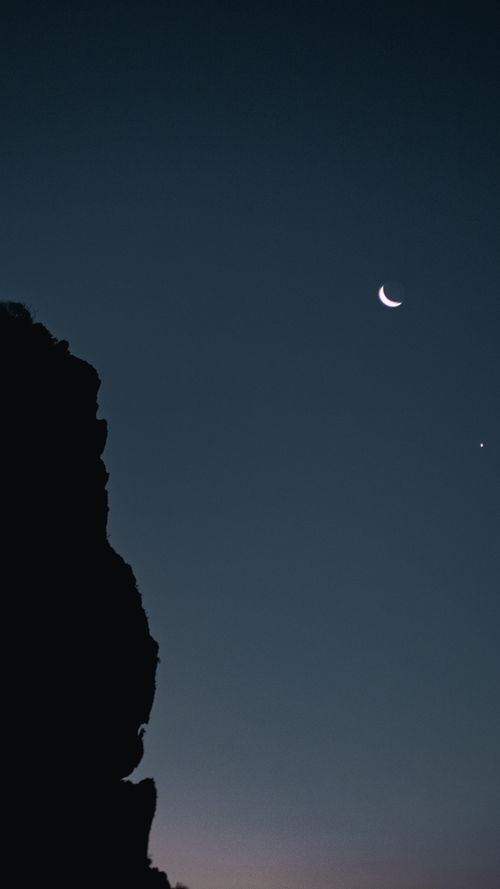 Free A beautiful crescent moon shines in a clear night sky above a silhouetted rock formation. Stock Photo