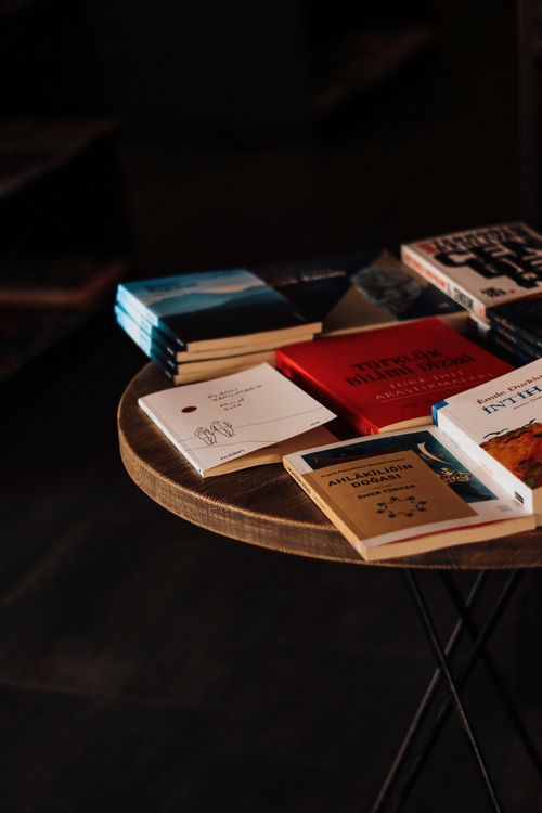 Free Collection of assorted books displayed on a wooden table in a cozy, dimly lit setting. Stock Photo