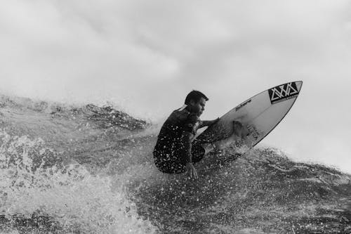 Black and white of fearless surfer riding on surfboard on splashing wave of stormy sea in tropical country during training