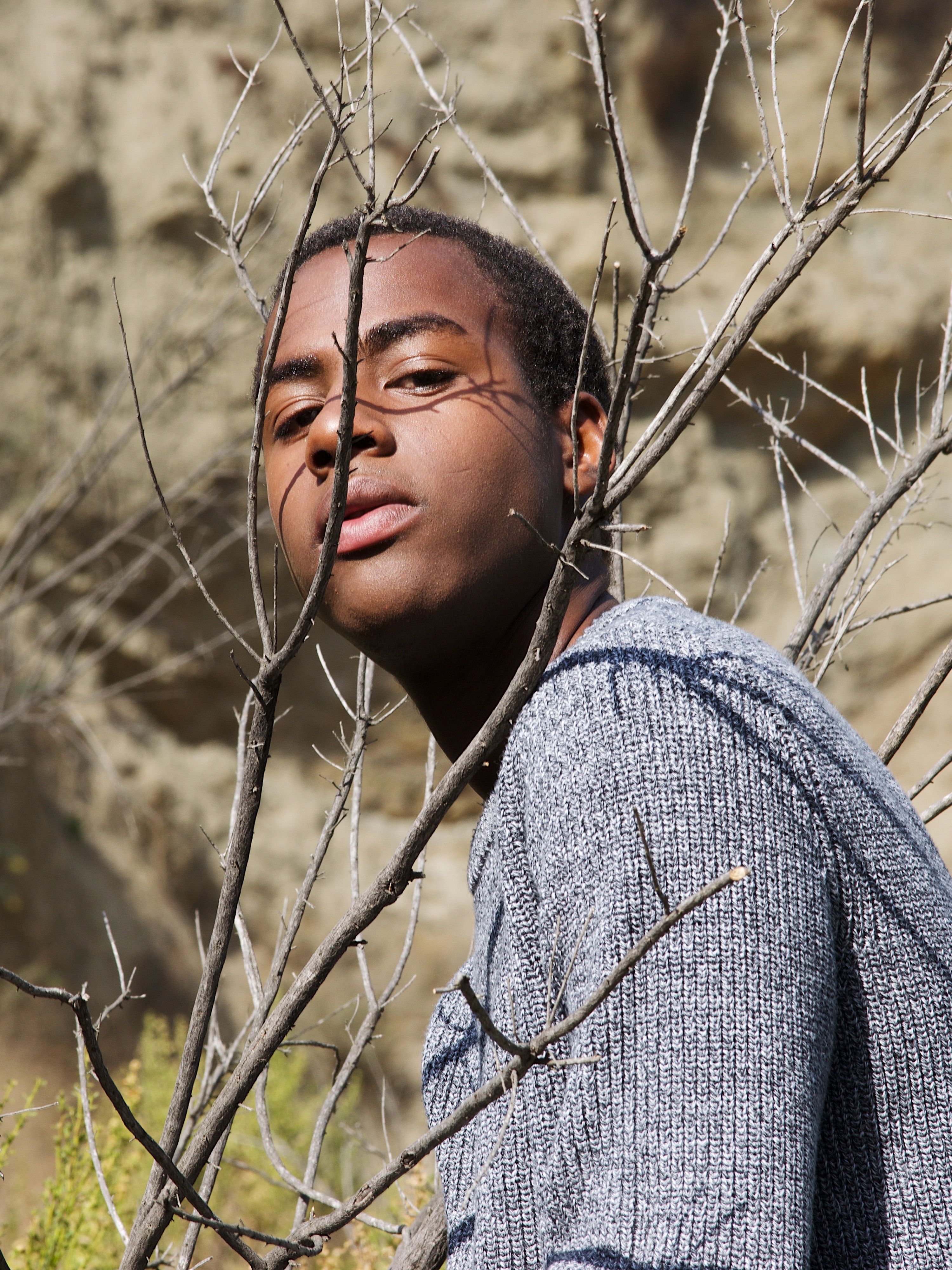 An artistic portrait of a man framed by bare branches in an outdoor setting.