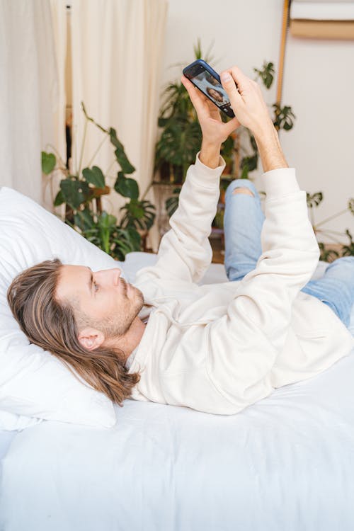 Free Man Lying on a Bed Using Cellphone Stock Photo