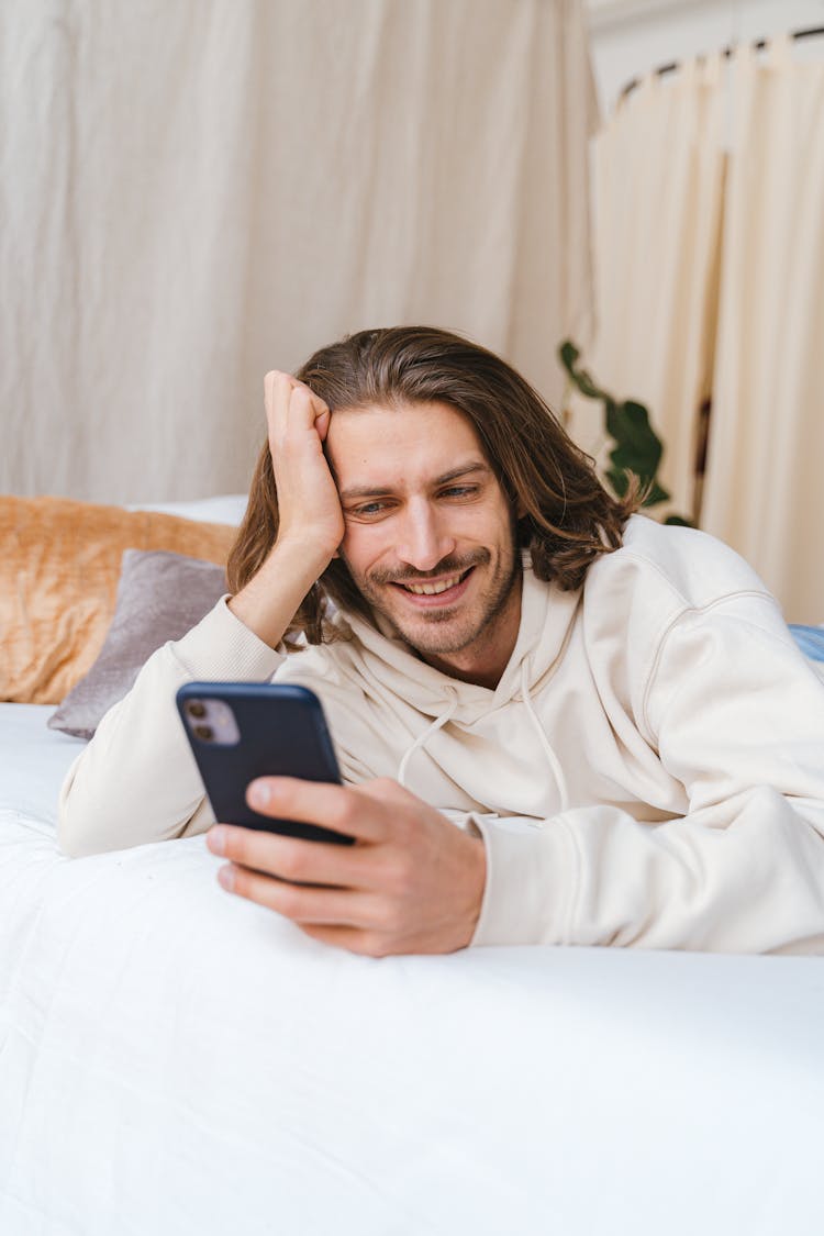 Man Lying On A Bed While Texting