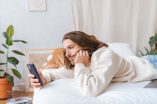 Free Good Looking Man Lying on a Bed Using a Cellphone Stock Photo