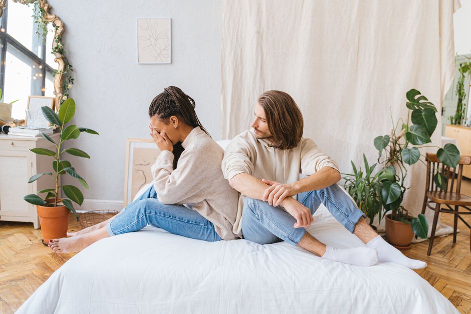 couple sitting back-to-back on a sofa looking exhausted - how burnout impacts couples couple sitting back-to-back on a sofa looking exhausted - how burnout impacts couples