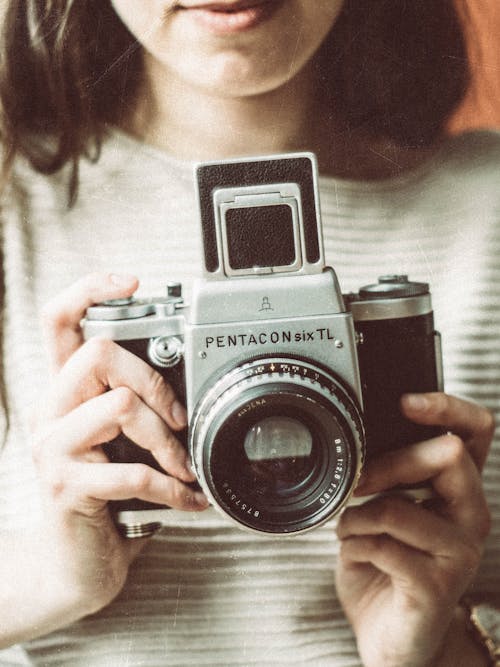 Crop unrecognizable young female photographer with long dark hair in casual clothes taking pictures on retro camera