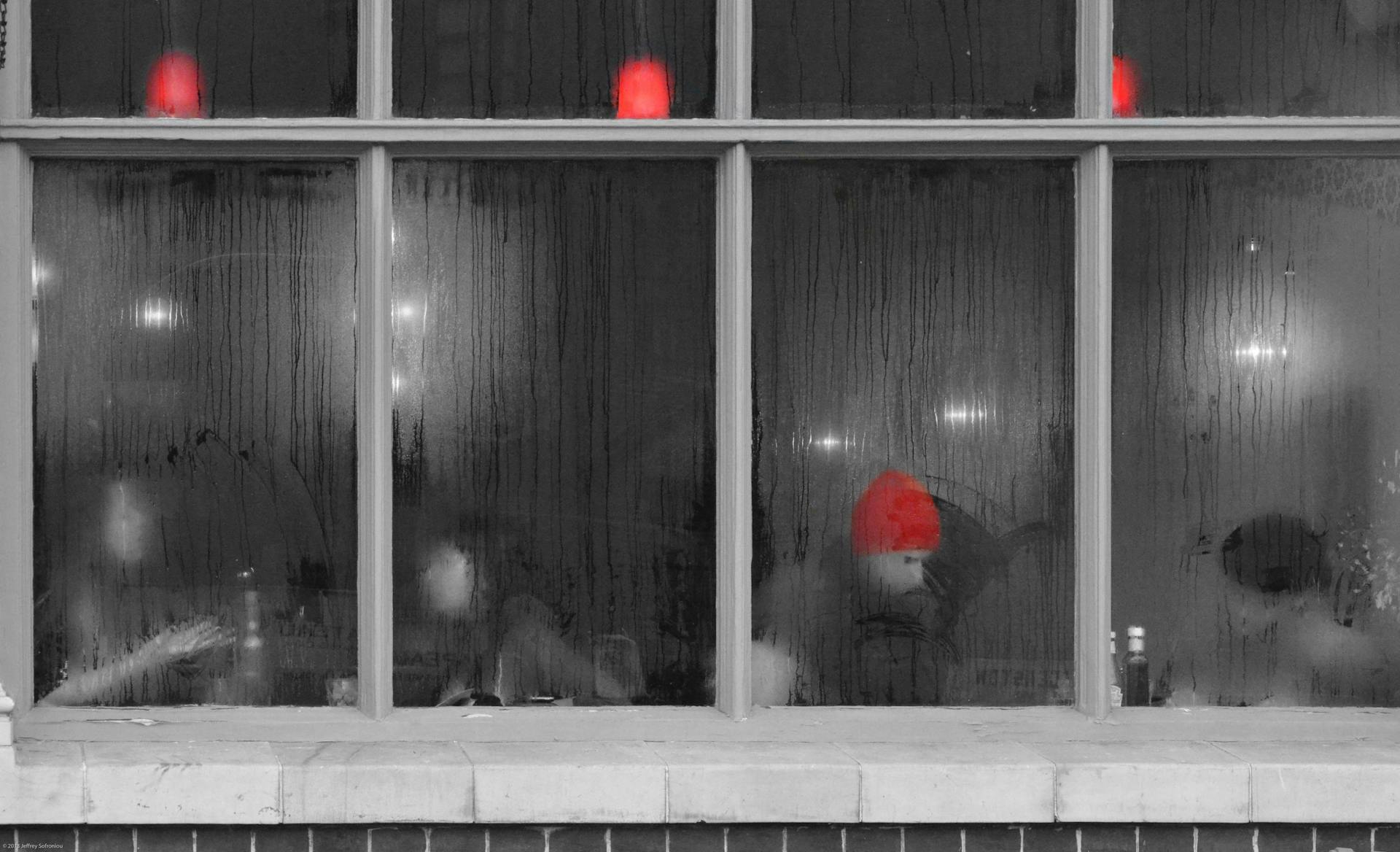 Steam-covered window in a London restaurant with a red hat visible, creating a cozy atmosphere.