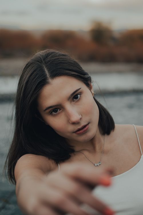 Free Close-up portrait of a young woman reaching towards the camera with a serene outdoor background. Stock Photo