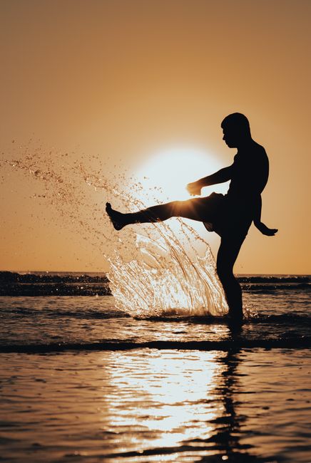 A silhouette of a man kicking water in the ocean during a stunning sunrise, capturing energetic movement and serene beauty. A silhouette of a man kicking water in the ocean during a stunning sunrise, capturing energetic movement and serene beauty.