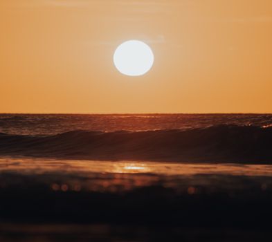 A serene sunset over the ocean with gentle waves under a warm, golden sky.