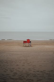 Red lifeguard station stands alone on a deserted beach with footprints in the sand.