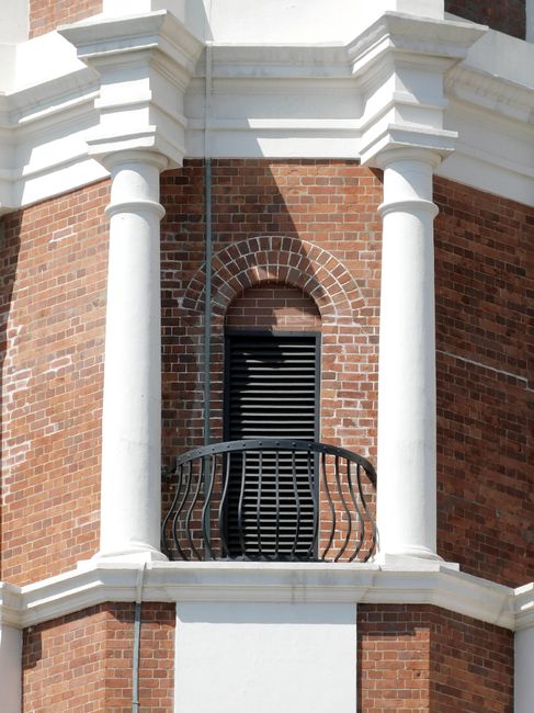 Facade of old building with brick walls and stone pillars with metal railing and decorative elements in city street in sunny day