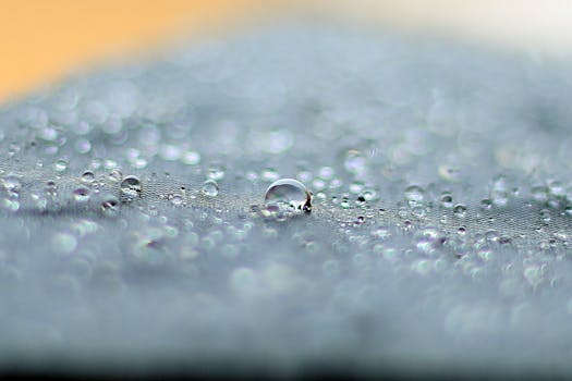 Close-up of dew droplets on a textured surface, glistening in natural light.