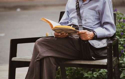 Free Elderly man enjoying leisure time reading a book on a bench outdoors. Stock Photo