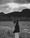 Fashionable young lady walking in field near mountains against misty sky