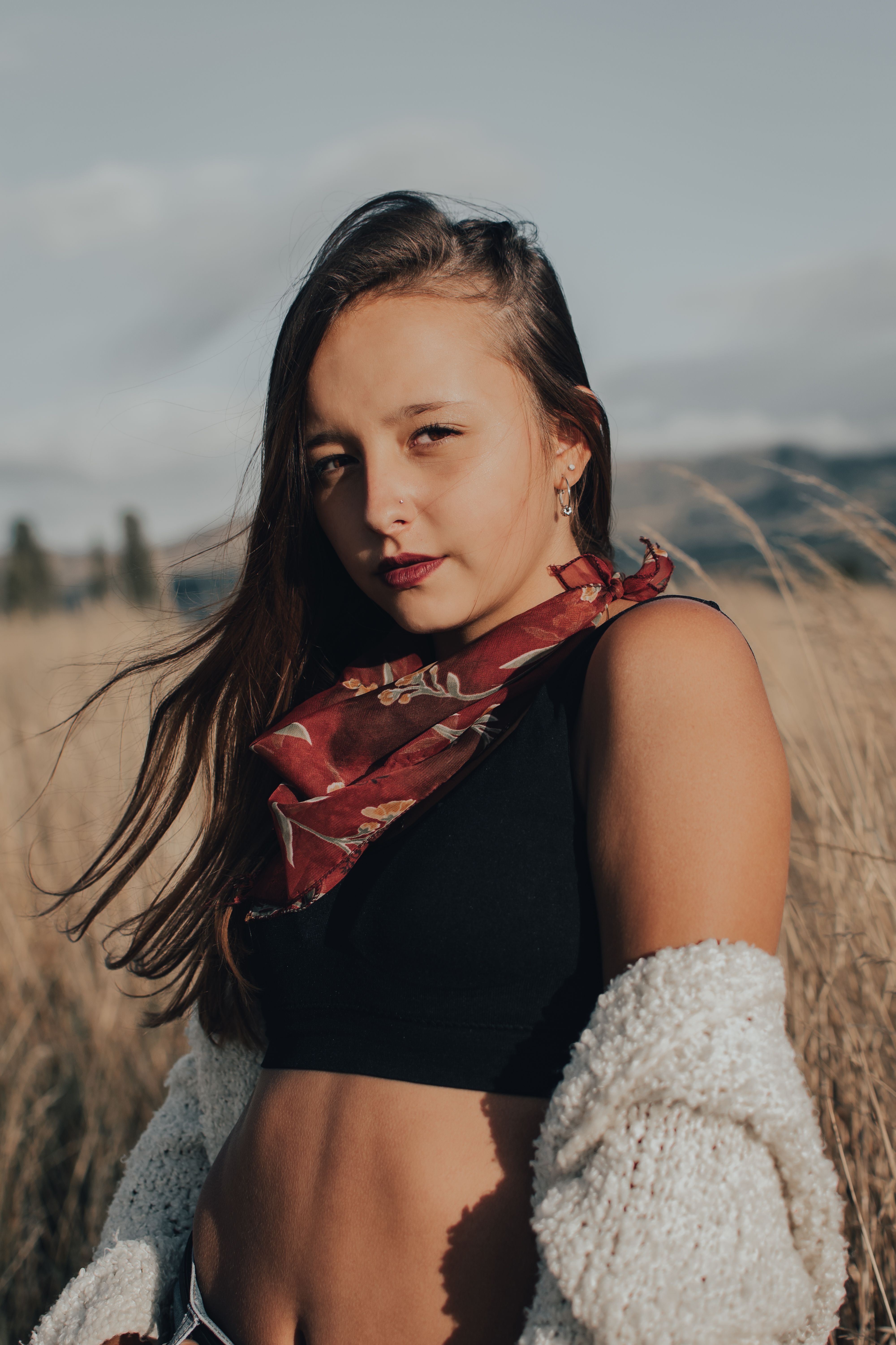 Portrait of a stylish young woman wearing a scarf outdoors in a grassy field.