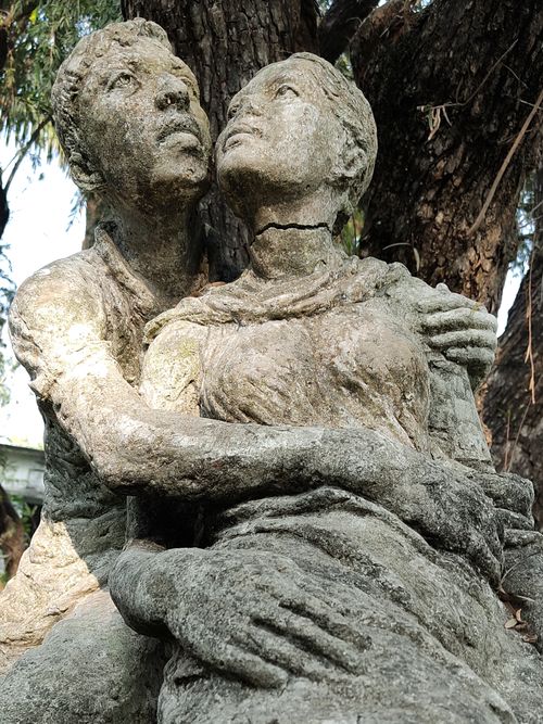Free Close-up of a weathered stone sculpture of a couple embracing in a sunlit park. Stock Photo