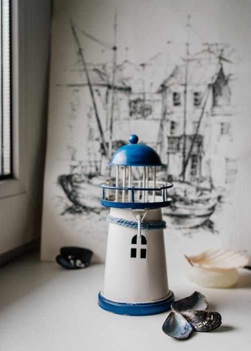 Miniature lighthouse composed with seashells and painting on table