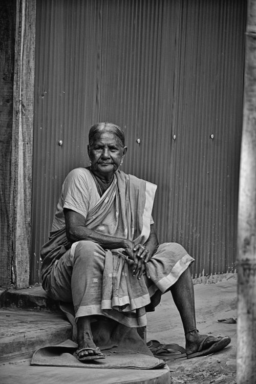 Free A black and white photo of an elderly woman in a saree sitting on steps outdoors. Stock Photo
