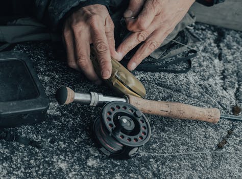 Detailed view of hands setting up a fishing reel with gear on a textured surface.