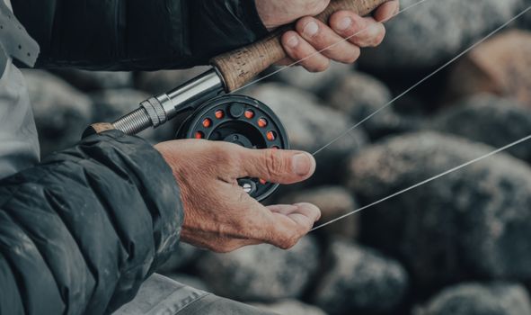 Detailed view of hands gripping a fishing rod with a reel, perfect for outdoor lifestyle and nature themes.