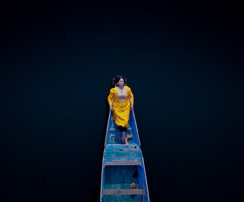 Drone shot of a woman in a yellow dress lying on a boat in Srinagar.