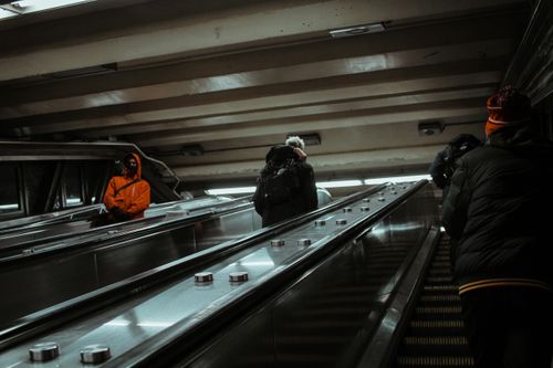 Free Crowd of people in warm outerwear standing on steps while riding contemporary escalator with metal handrails in modern subway station Stock Photo