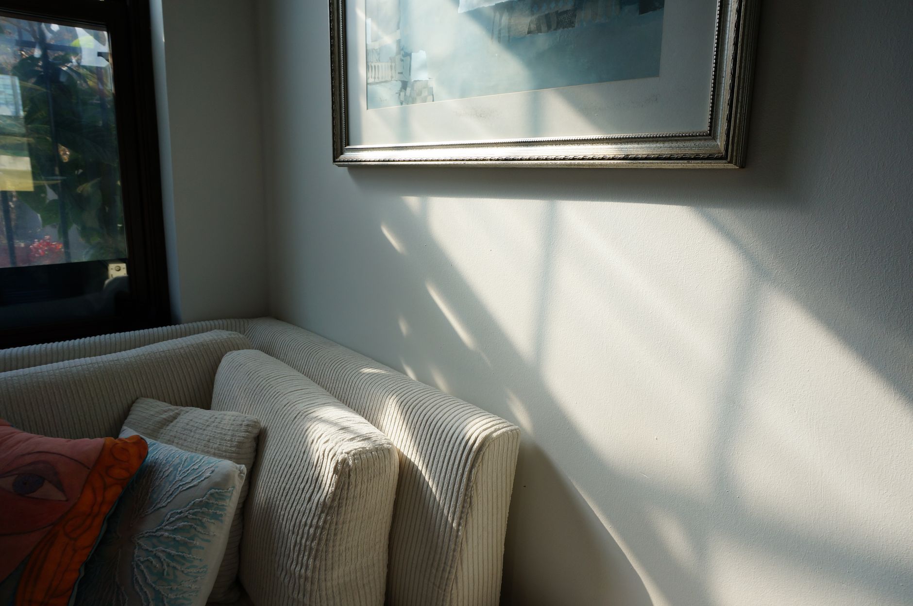 A serene living room corner with a couch and pillows, bathed in soft sunlight.