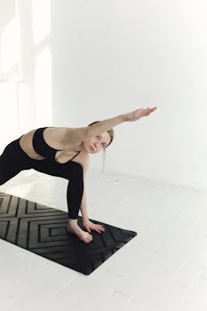 Woman performing yoga pose on a mat indoors, emphasizing flexibility and healthy lifestyle.