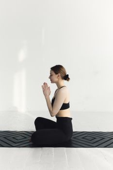 A woman in activewear meditating on a yoga mat indoors, embodying serene wellness.