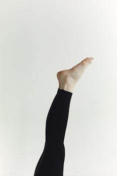 A minimalist photo of a person's leg in black pants raised against a white background, showcasing flexibility.